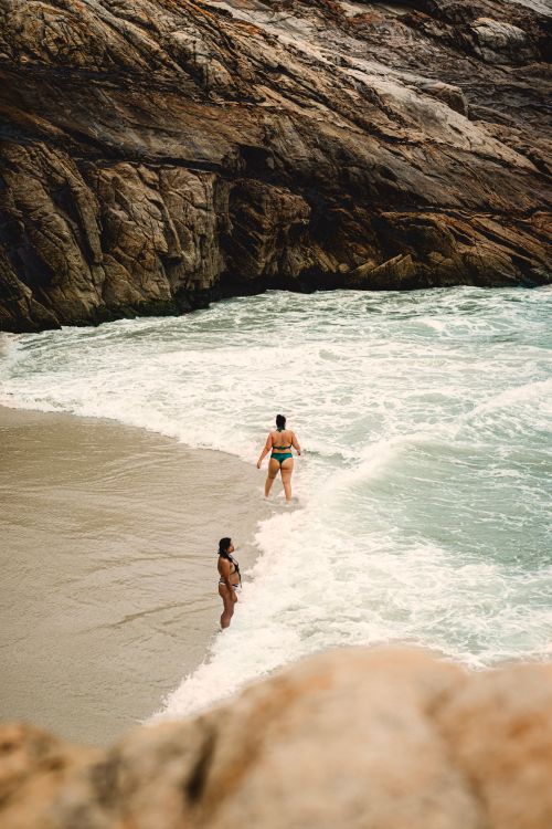 Free Two people enjoying a swim near rocky cliffs at a picturesque beach. Stock Photo