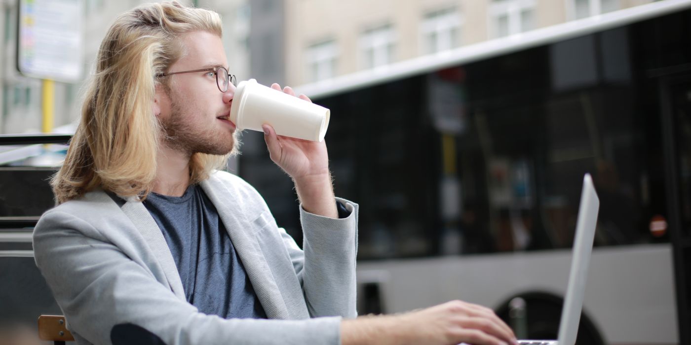 Young man working remotely on laptop while enjoying a coffee outdoors.