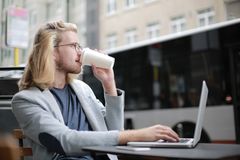 Young man working remotely on laptop while enjoying a coffee outdoors.