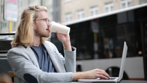 Young man working remotely on laptop while enjoying a coffee outdoors.