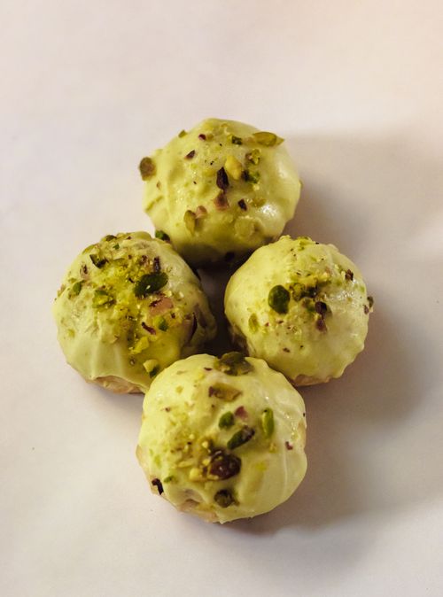 Free Close-up of four pistachio-covered pastry balls on a light background, showcasing their texture and topping. Stock Photo