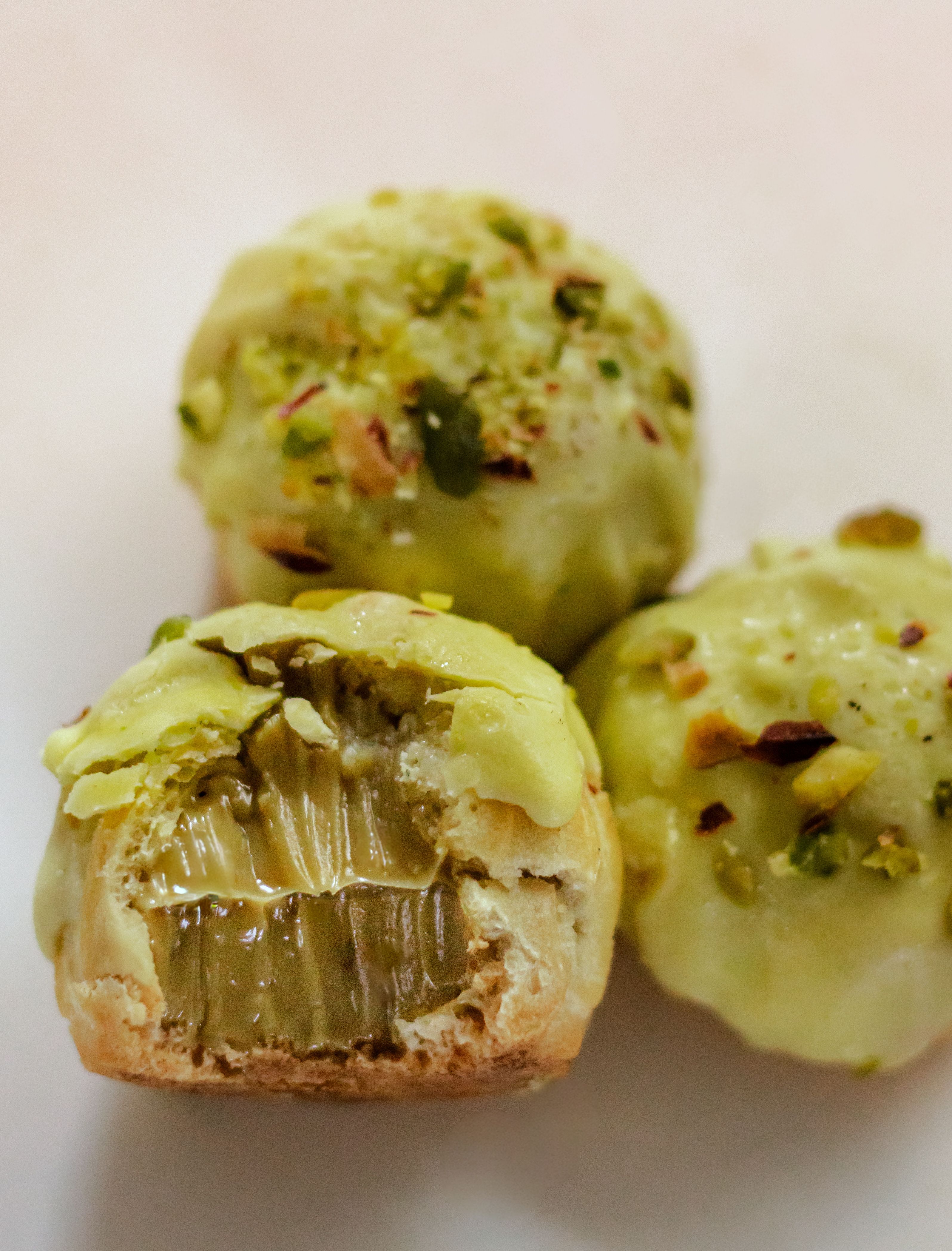 Close-up of three pistachio-topped cream puffs with creamy filling, a delightful dessert treat.