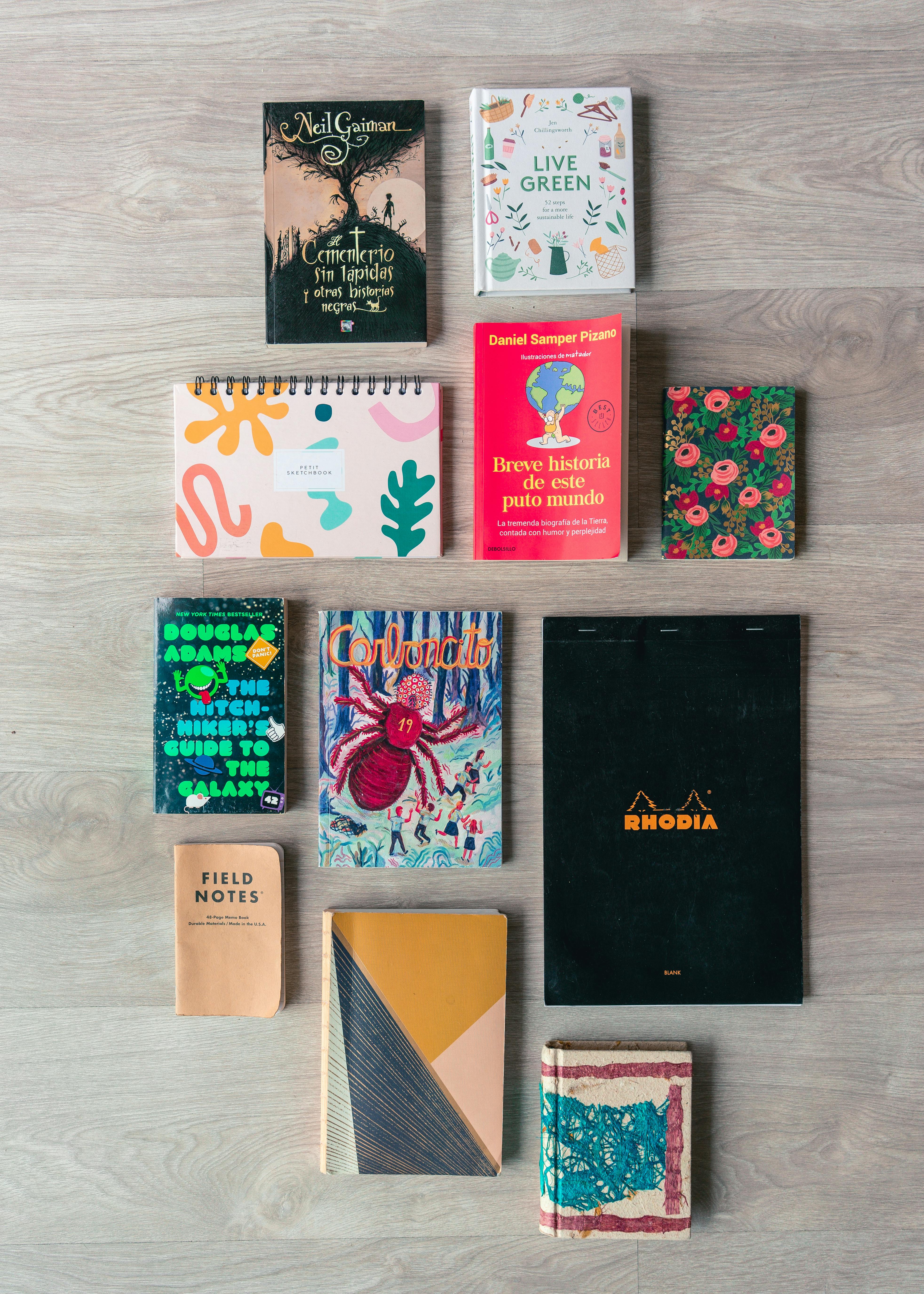 A vibrant flat lay of books and notebooks on a wooden surface, showcasing diverse designs and genres.
