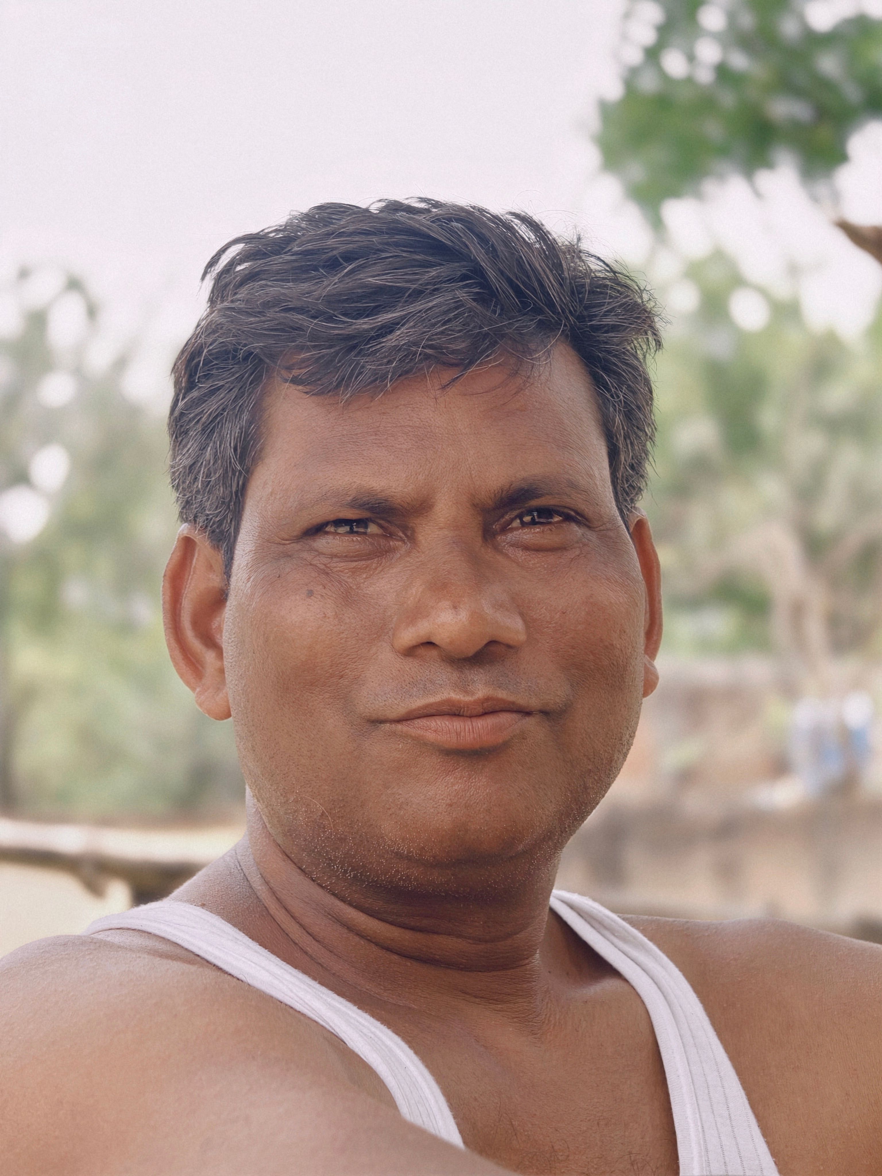 Close-up portrait of a man outdoors in a casual white tank top with a natural background.