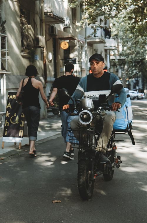 Free Delivery cyclist on a city street with pedestrians and urban backdrop, evoking a lively urban environment. Stock Photo