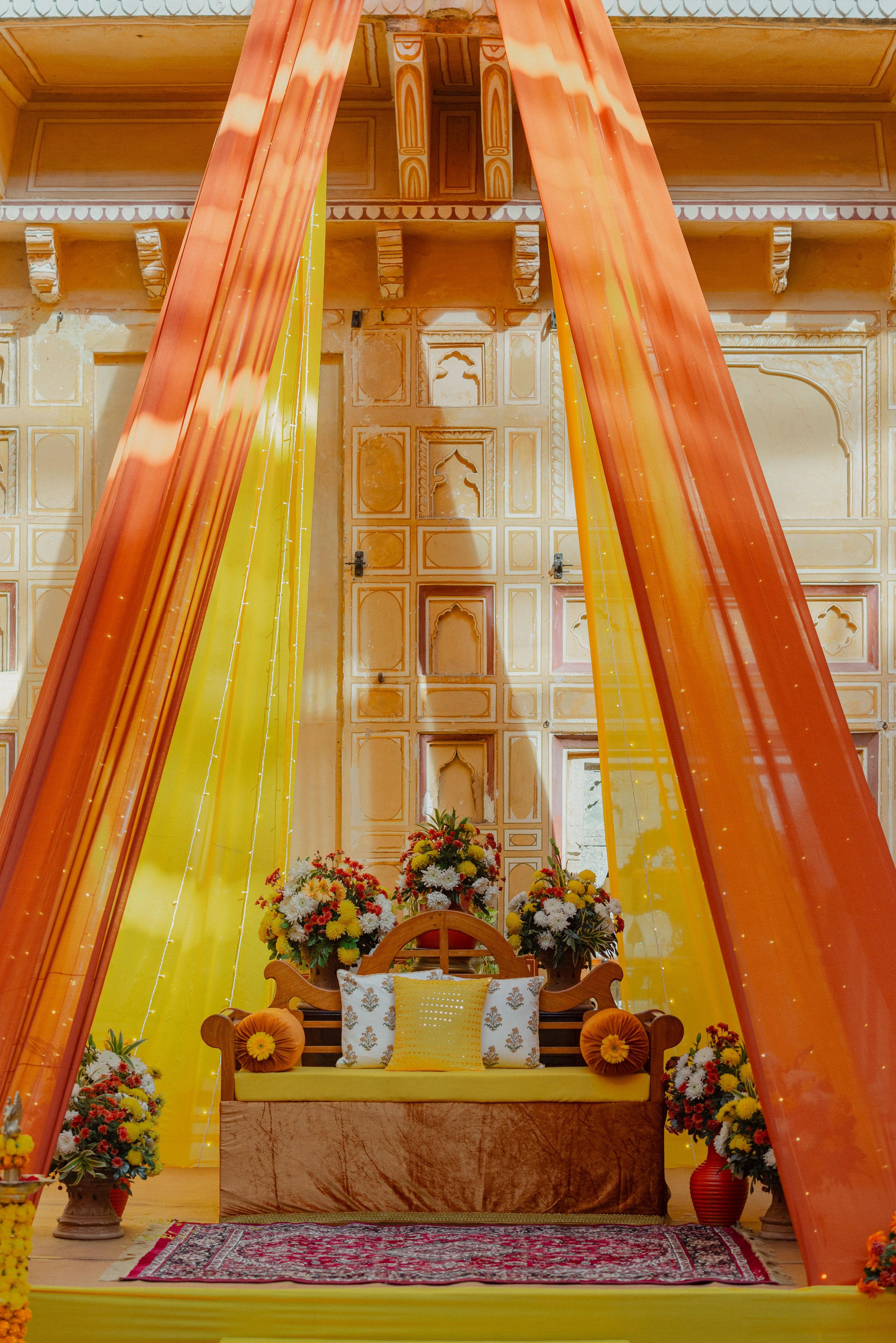 Saffron and gold drapery with floral arrangements on a traditional wedding stage