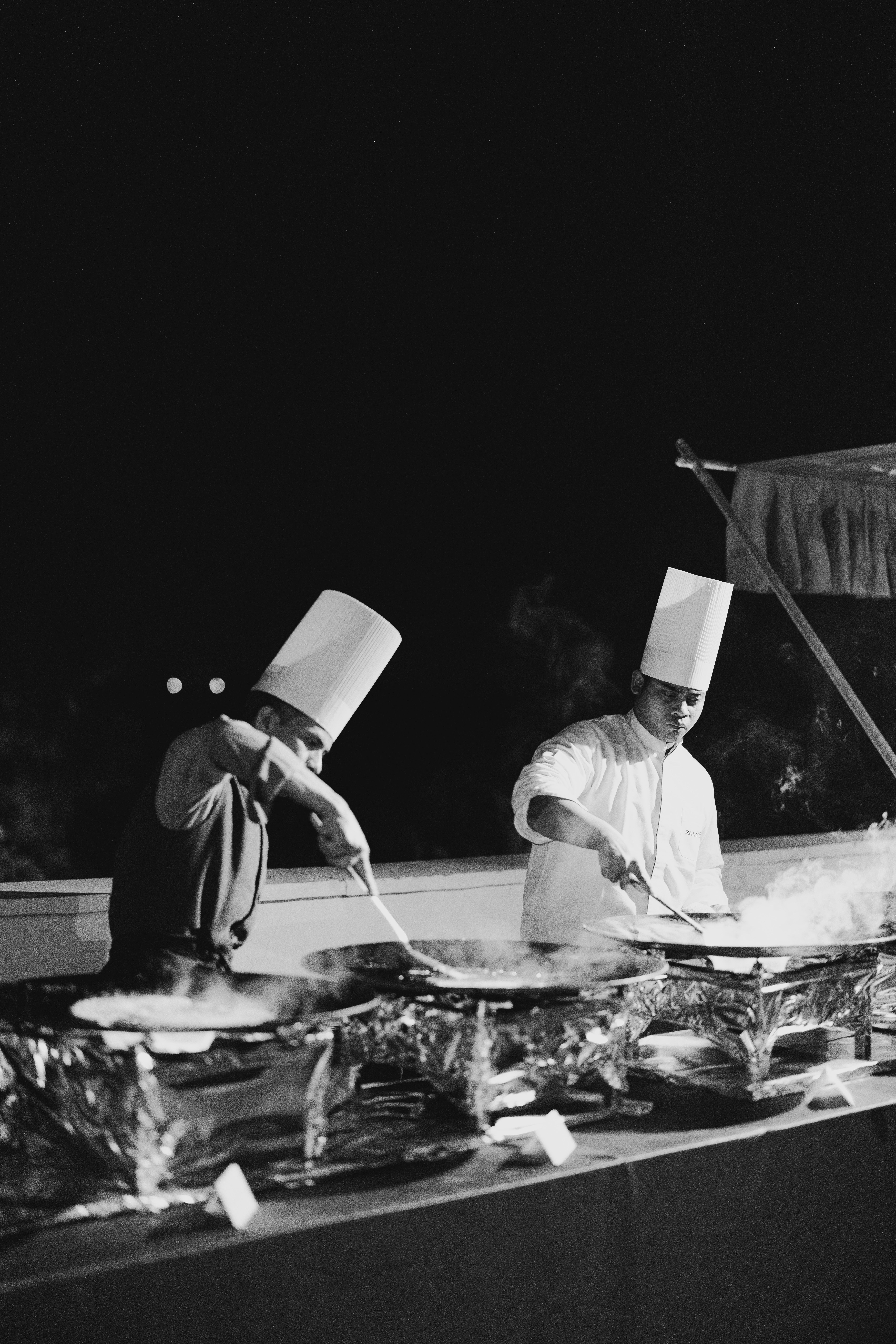 Two chefs cooking outdoors at night in black and white photography.