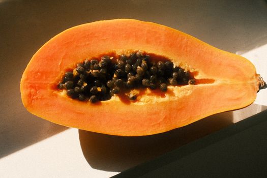 A ripe papaya split open, revealing seeds, bathed in natural sunlight.