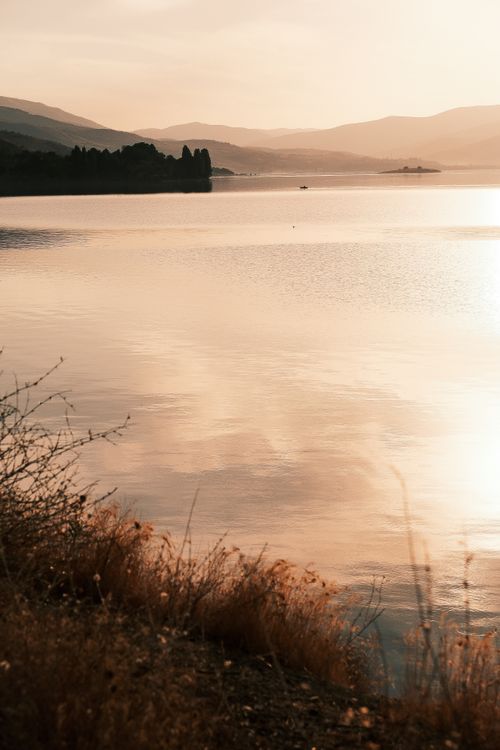 Free Peaceful sunset by a lake surrounded by silhouetted hills, with reflection on calm water. Stock Photo