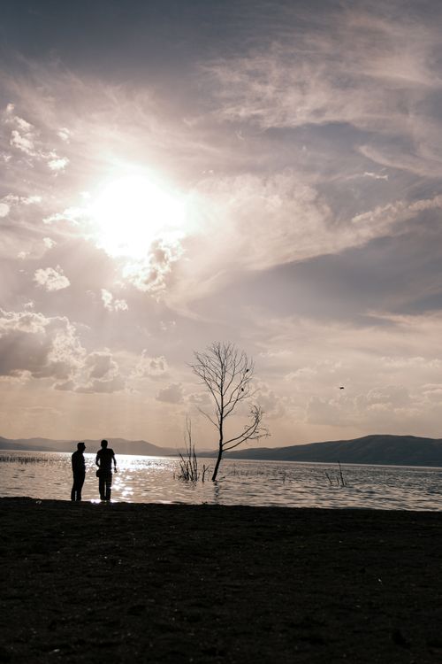 Free Two people stand silhouetted against a serene lake during sunset, creating a tranquil scene. Stock Photo