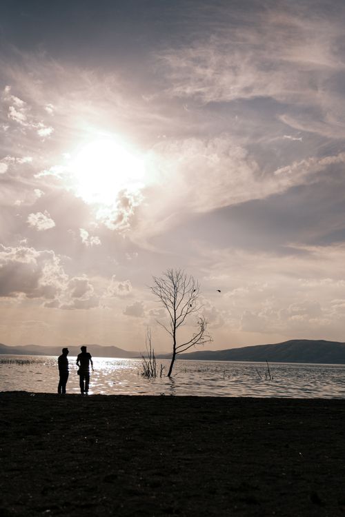 Free Two people silhouetted by a tranquil lake at sunset with a picturesque sky. Stock Photo