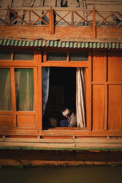 Free An elderly man peacefully sitting inside a wooden houseboat by the water. Stock Photo