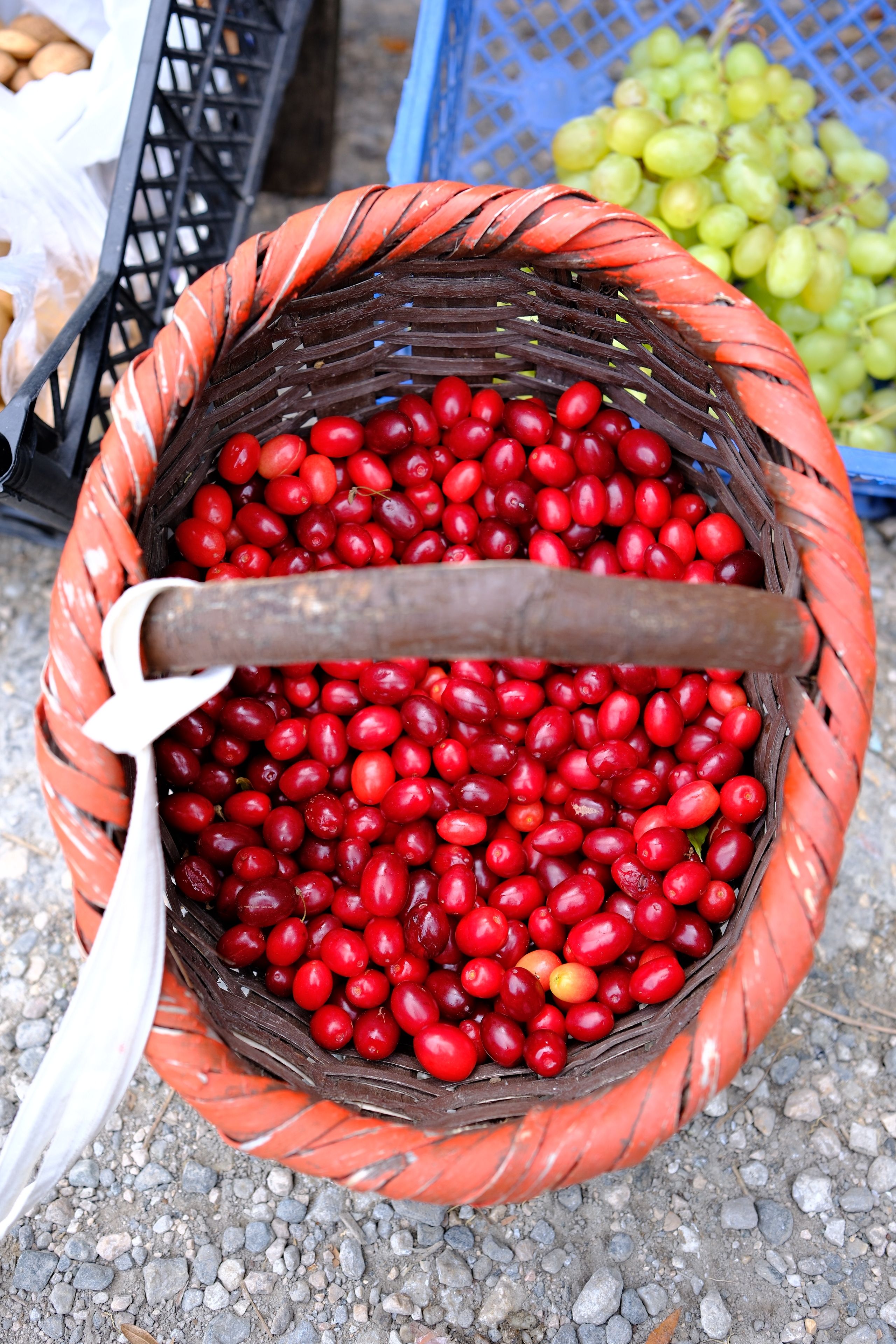A rustic basket filled with vibrant red dogwood fruit at an outdoor market in Orhaneli, Türkiye.