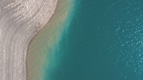 Free A stunning aerial view of turquoise water meeting a gravel shoreline, highlighting natural textures. Stock Photo
