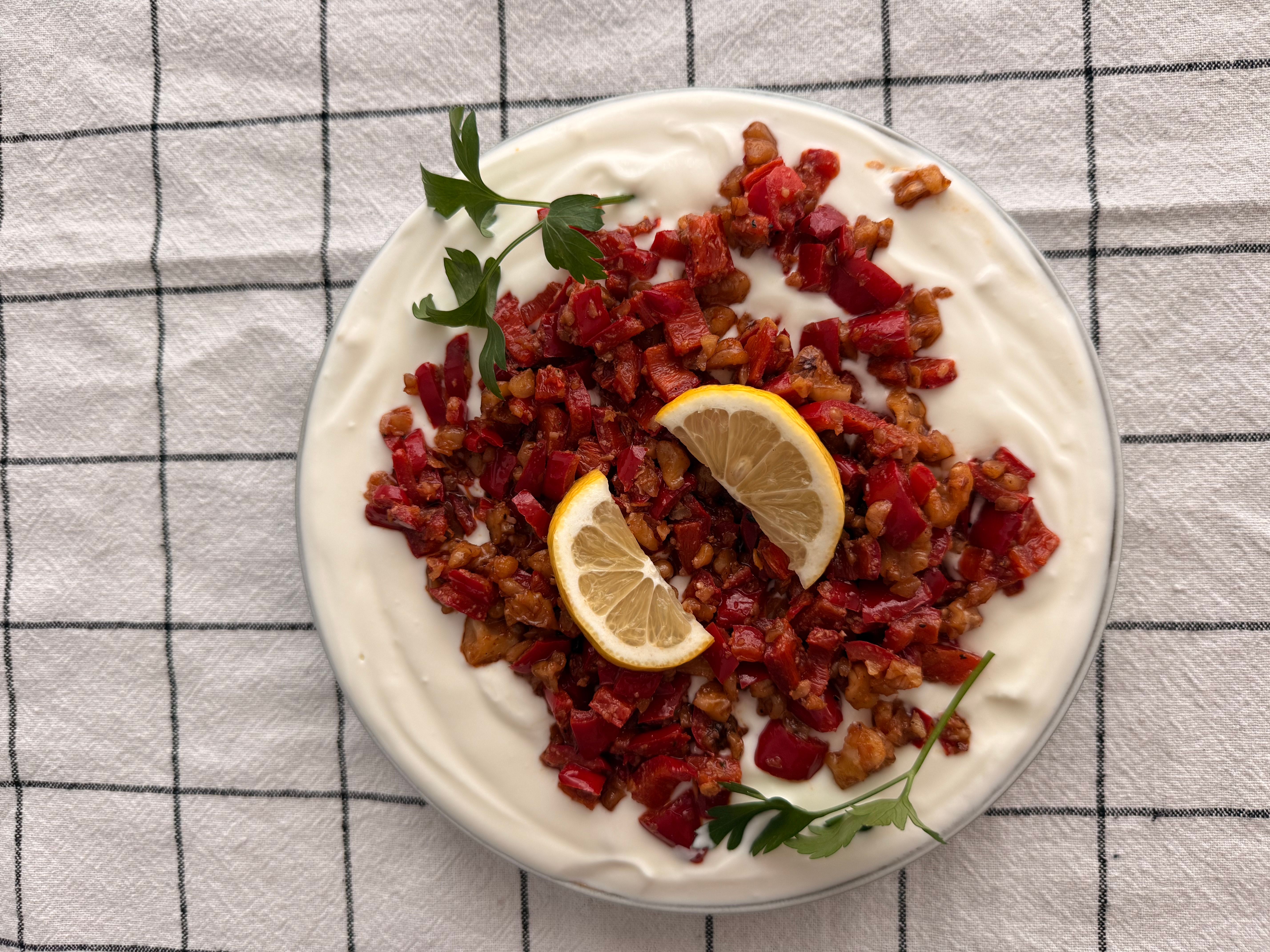 Top view of a delicious Turkish meze with yogurt, red peppers, and lemon slices, served on a grid-patterned tablecloth.