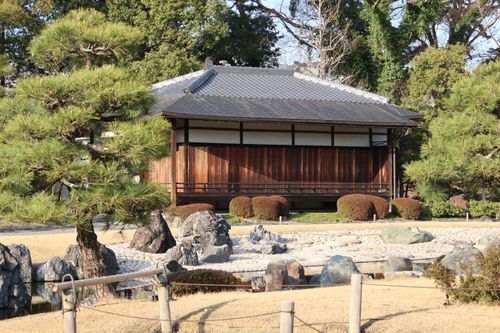 Free Serene view of a Japanese garden featuring a traditional wooden house and manicured landscape. Stock Photo