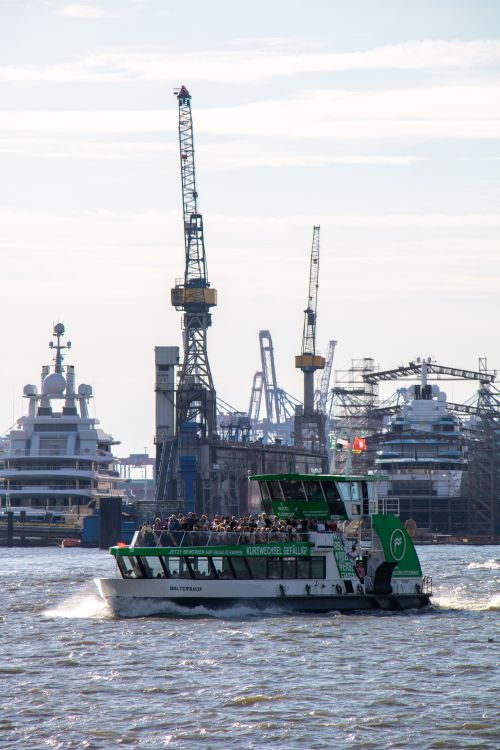 Free A passenger ferry sails on the Elbe River with cranes and ships in Hamburg harbor on a sunny day. Stock Photo