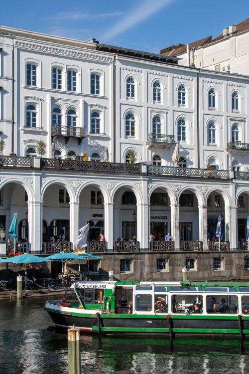 Free Elegant white buildings of Alsterarkaden overlooking a canal in Hamburg with a passing boat. Stock Photo