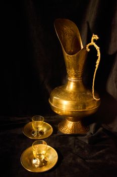 A vintage brass pitcher with two cups on a dark background, highlighting their intricate design.