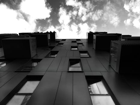 一张低角度拍摄的黑白照片，展现了一座现代建筑和戏剧性的云层