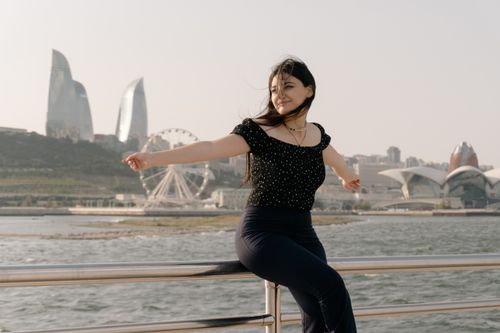 Free A joyful woman sitting by the Caspian Sea with Baku's skyline in the background, enjoying a breezy day. Stock Photo