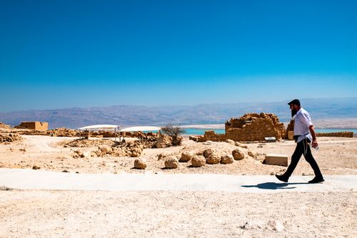 Free A man walks near ancient ruins of Masada, Israel on a sunny day with Dead Sea in the background. Stock Photo