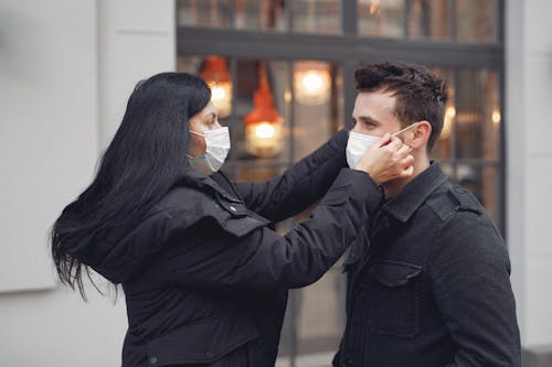 Young careful couple adjusting medical masks against urban building