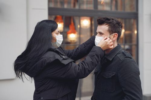 Free Side view of woman in warm outerwear adjusting protective mask on face of man on city street in cold season during coronavirus pandemic while looking at each other Stock Photo