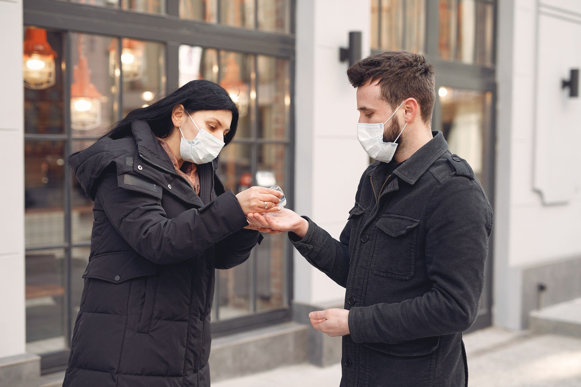 A man and woman wearing masks using hand sanitizer outdoors for hygiene during COVID-19.