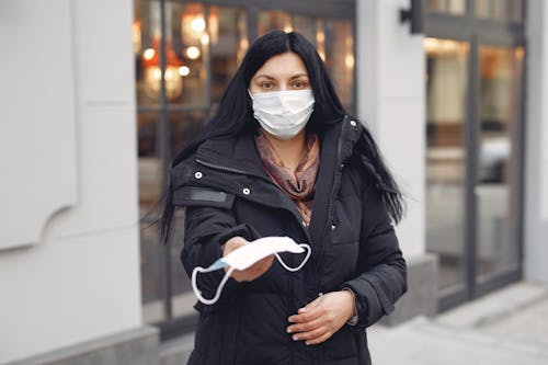 Young woman wearing medical mask and black down jacket on urban street in cold season