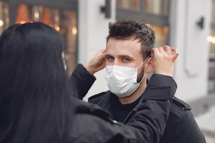 Young Couple Adjusting Medical Mask Against Blurred Urban Building