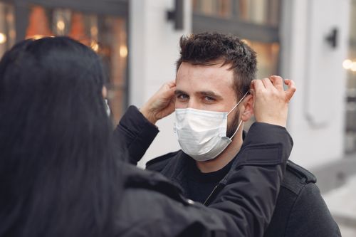 Free Concerned woman in warm outerwear adjusting protective mask on face of bearded man on city street in cold season during coronavirus pandemic Stock Photo