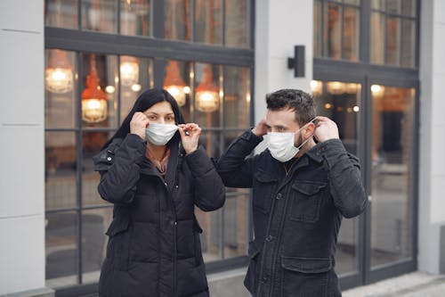 Young couple adjusting medical masks against urban building exterior