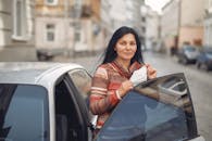 Content young woman with medical mask in hands standing near car on urban street