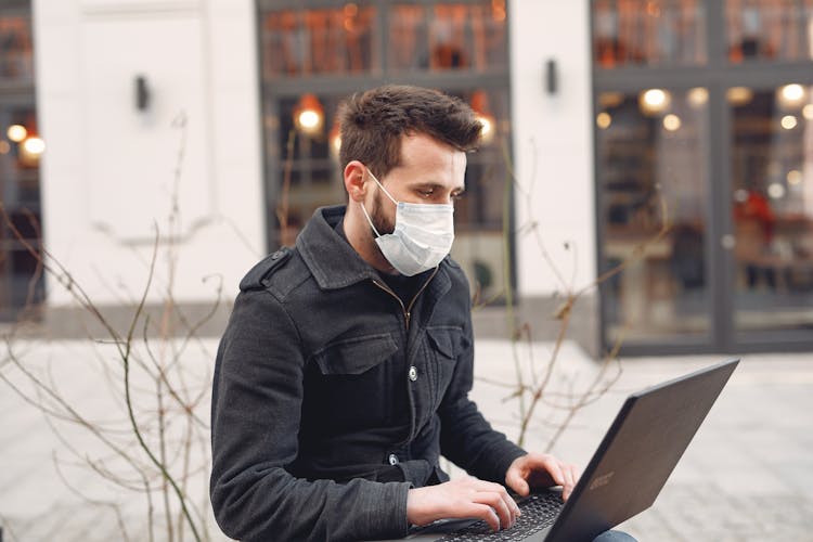 Focused Businessman In Medical Mask Using Laptop On Urban Street