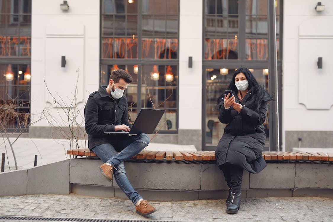 Young couple wearing medical masks with laptop and smartphone on city street