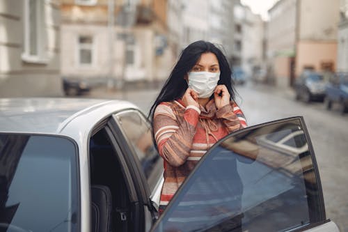Young woman wearing medical mask standing near automobile on empty urban street