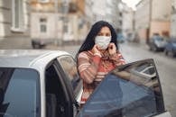 Young woman wearing medical mask standing near automobile on empty urban street