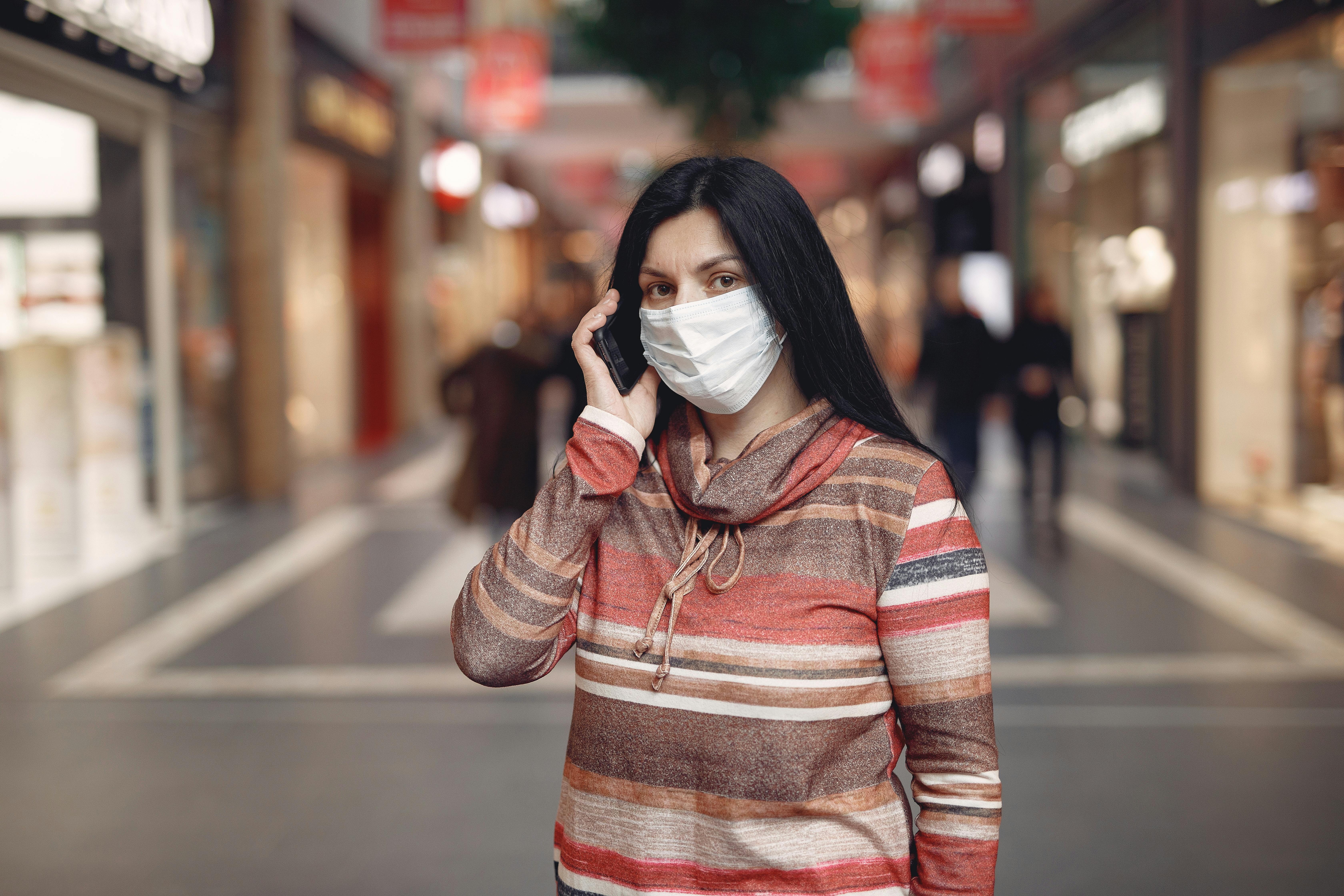 serious ethnic female in mask talking on mobile phone in modern building