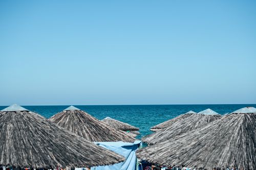 Free A serene beach view featuring straw umbrellas overlooking a clear blue sea and sky. Stock Photo