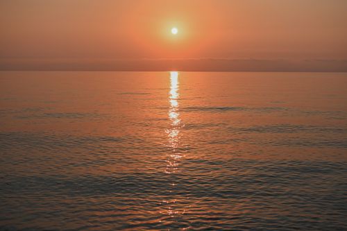 Free A tranquil sunset over calm ocean waters with a warm, reflective glow. Stock Photo