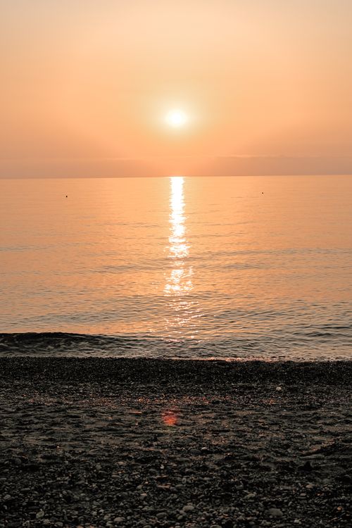 Free Sunrise casting warm reflections over a serene beach and calm sea. Stock Photo