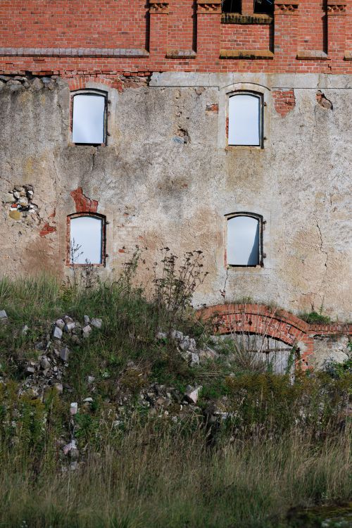 Free A decaying brick building facade with broken windows and overgrown vegetation in Sovetsk, Russia. Stock Photo