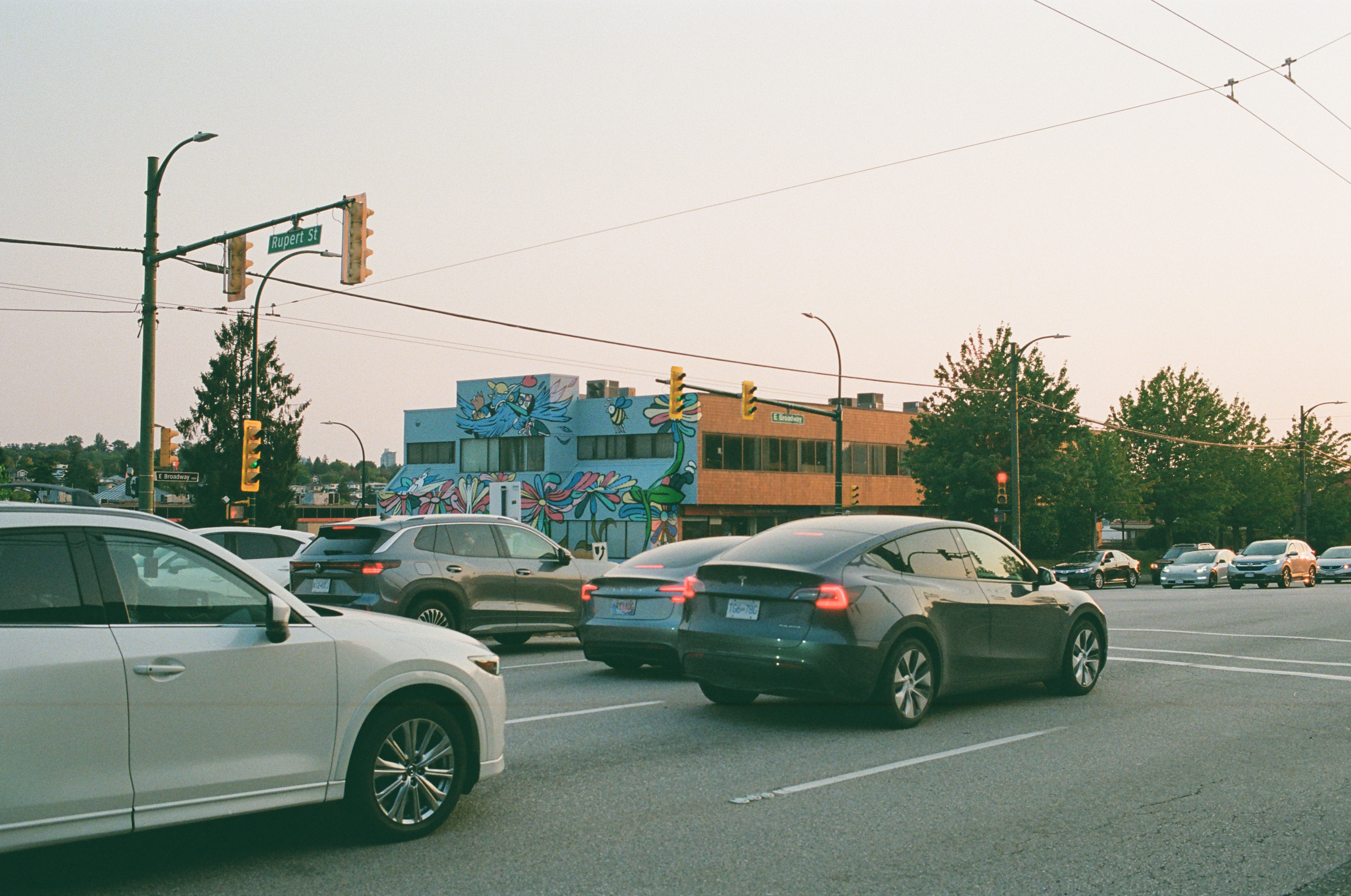 City intersection at sunset featuring cars, traffic lights, and a colorful mural.