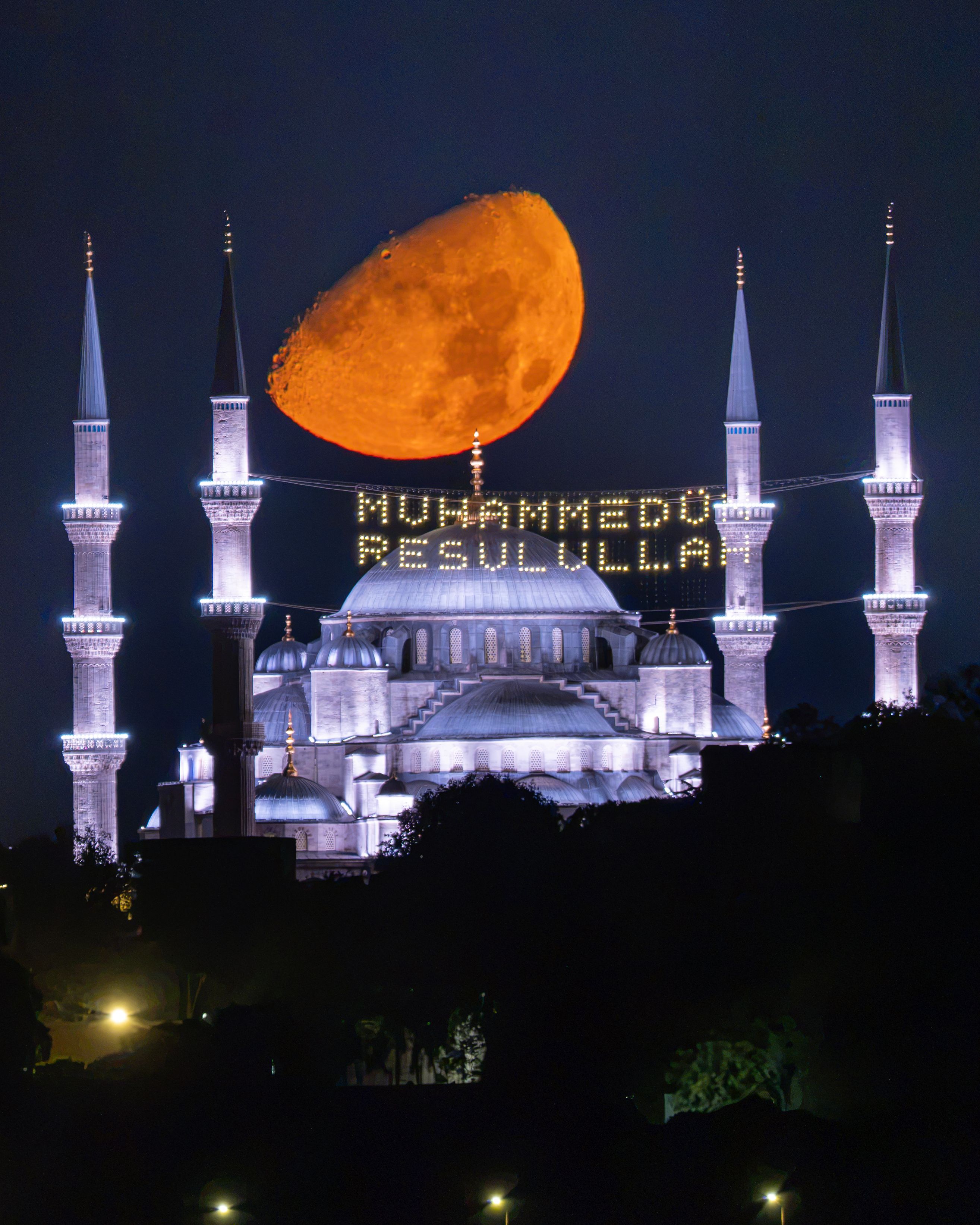 A stunning view of the moon rising over Istanbul's iconic Blue Mosque illuminated at night.