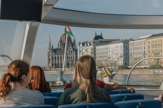 Tourists on a river cruise boat admire the Budapest Parliament Building on a sunny day.