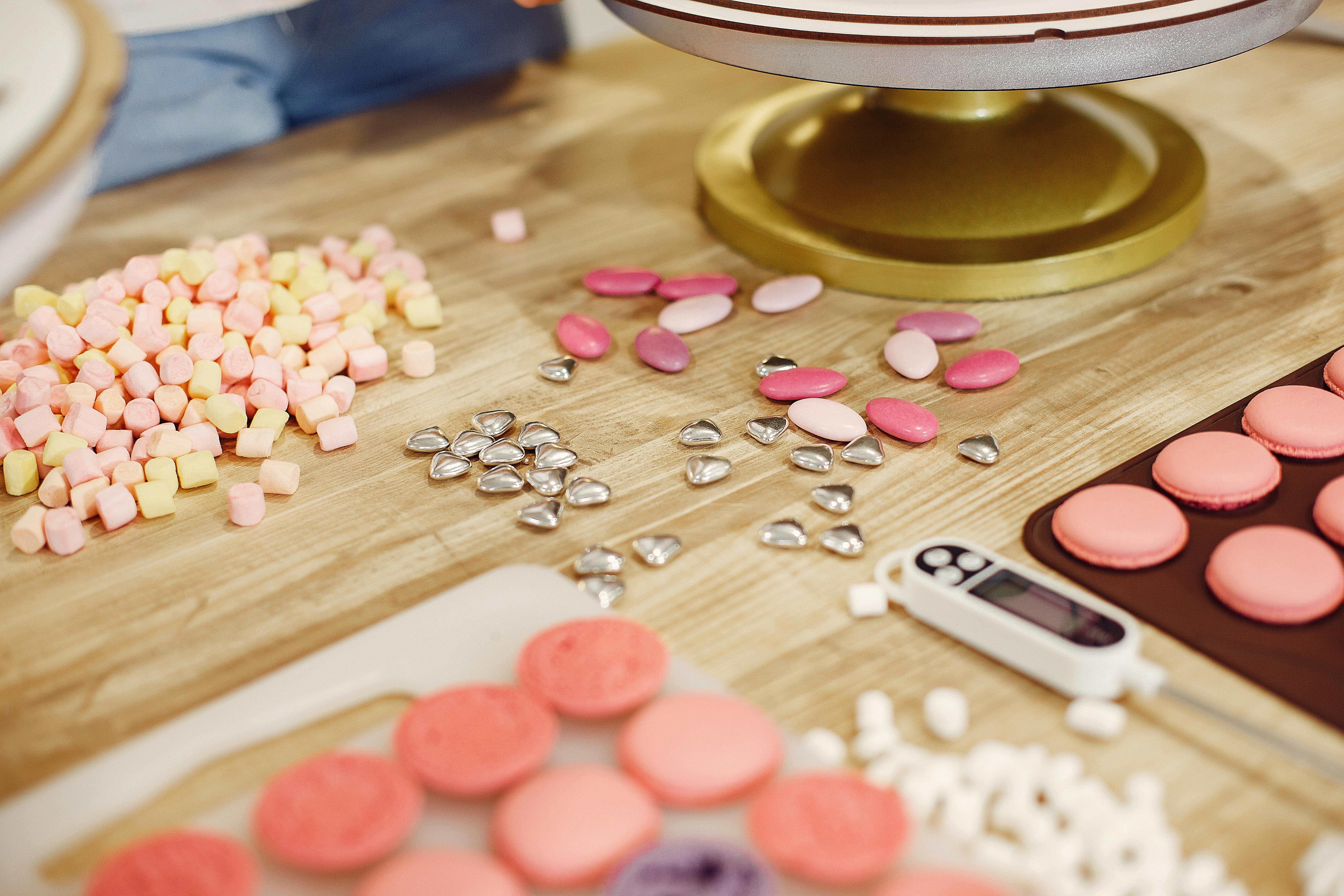 Table with various shiny sprinkles placed near mat of macaroons and cooking thermometer in process of making delicious desserts in restaurant