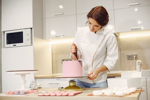 Concentrated female pastry cook decorating cake with pleasure in modern restaurant