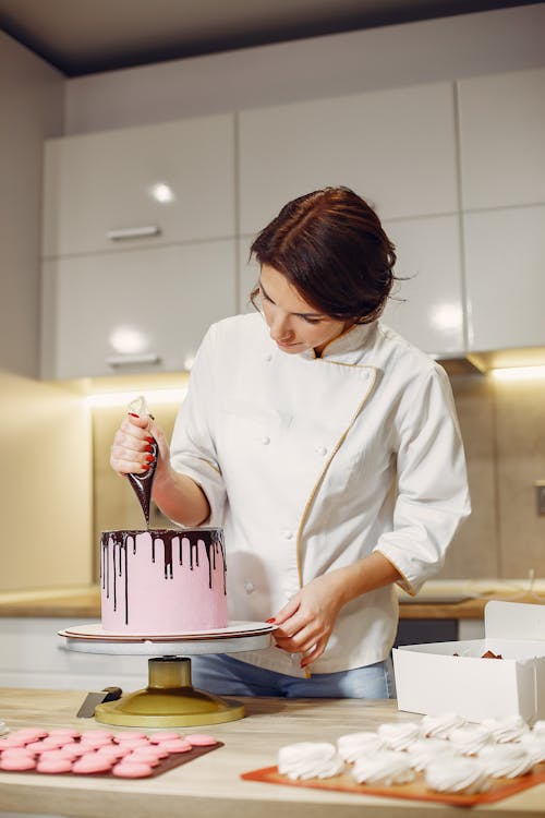 Free Female confectioner decorating cake with chocolate in contemporary kitchen Stock Photo