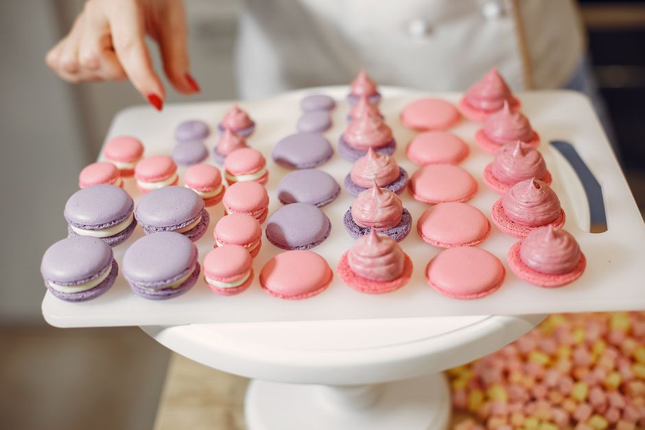 A vibrant display of pink and purple macarons being crafted in a kitchen setting.